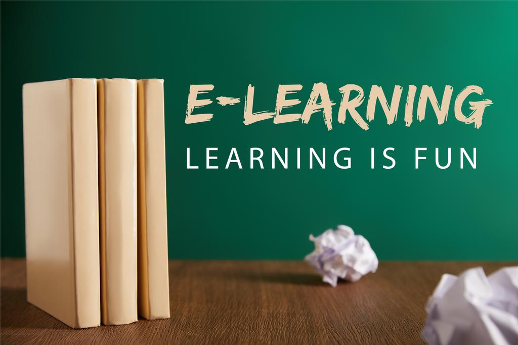 τρία βιβλία και τσαλακωμένο έγγραφα στο ξύλινο τραπέζι με την επιγραφή «e-learning - μάθηση είναι διασκέδαση» - Φωτογραφία, εικόνα