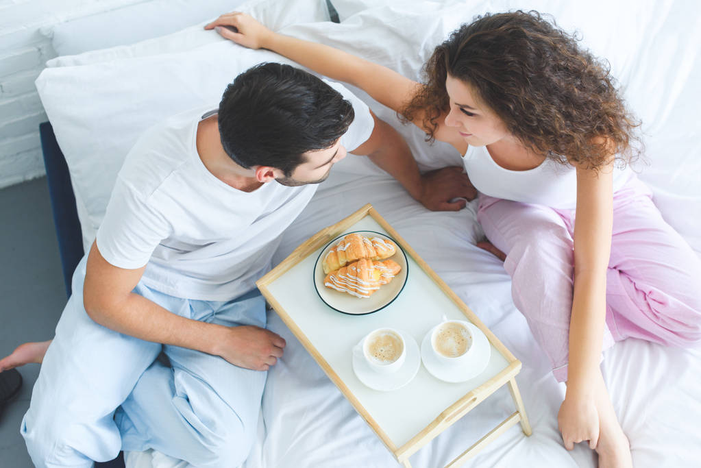 overhead view of young couple in pajamas having breakfast together in bed  - Photo, Image