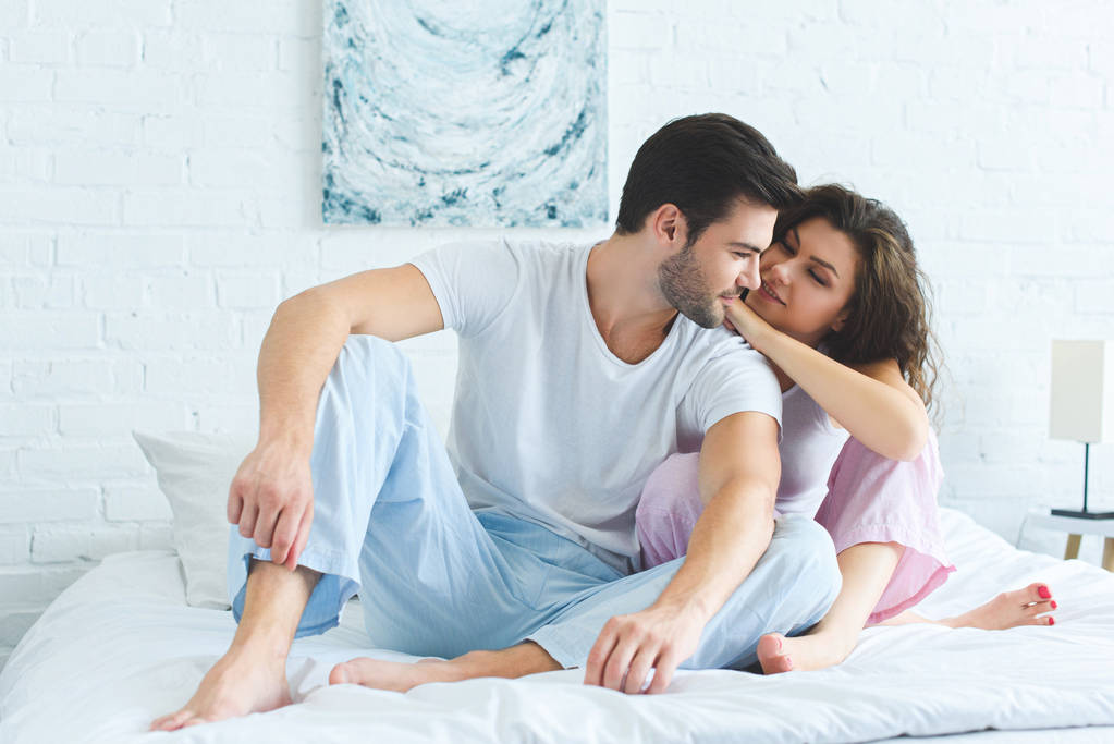 красива усміхнена молода пара в піжамі сидить разом на ліжку
 - Фото, зображення