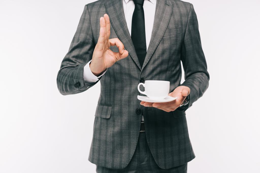 abgeschnittenes Bild eines Geschäftsmannes, der eine Tasse Kaffee in der Hand hält und eine auf Weiß isolierte Geste zeigt - Foto, Bild