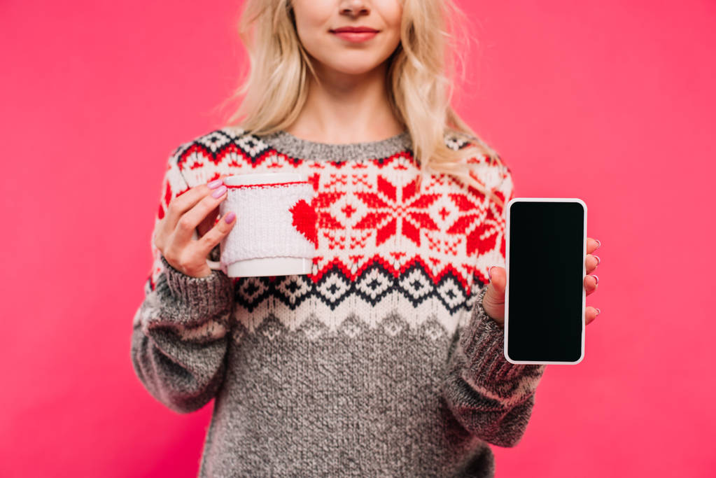 körülvágott kép holding kupa és okostelefon üres képernyő elszigetelt rózsaszín pulóver lány - Fotó, kép