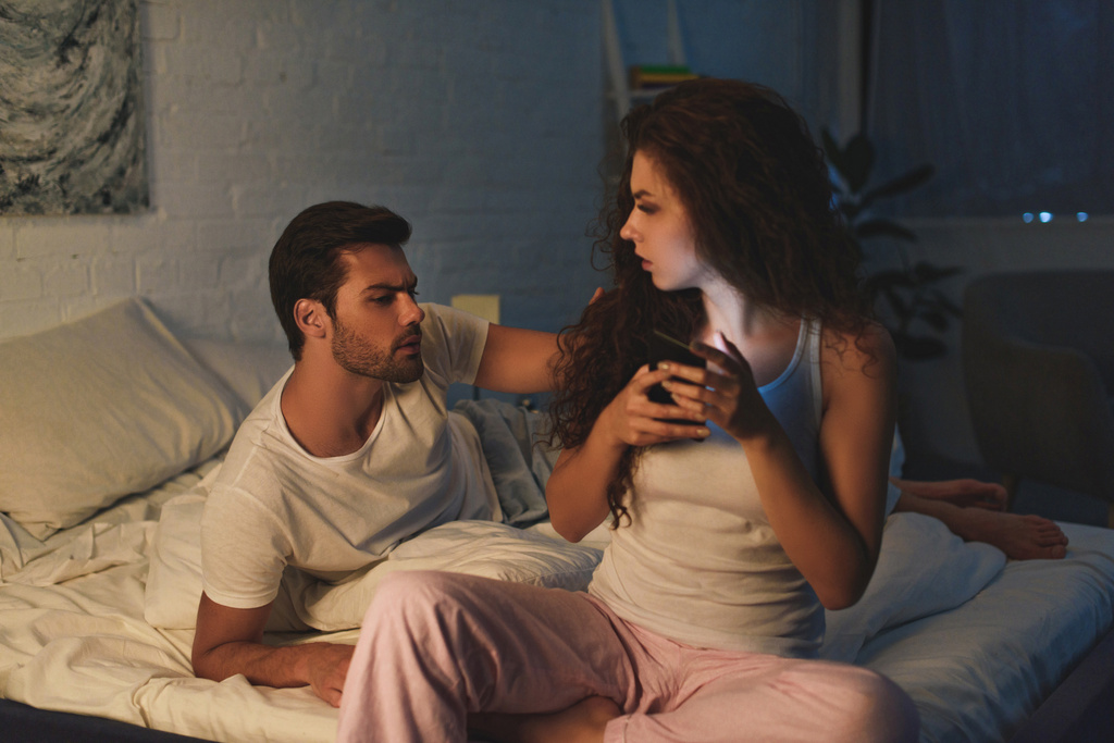 Verärgerter junger Mann schaut Freundin nachts mit Smartphone an, Beziehungsschwierigkeiten  - Foto, Bild