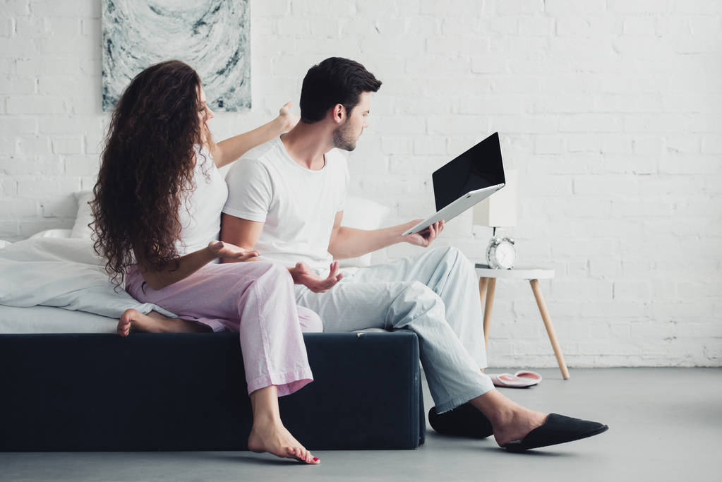 jeune femme en colère regardant petit ami à l'aide d'un ordinateur portable avec écran blanc, concept de difficultés relationnelles
 - Photo, image