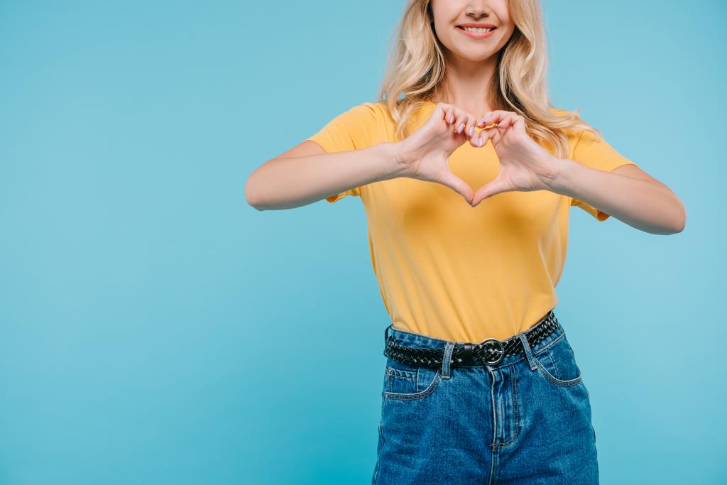 bijgesneden afbeelding van meisje in shirt en broek hart tonen met handen geïsoleerd op blauw - Foto, afbeelding