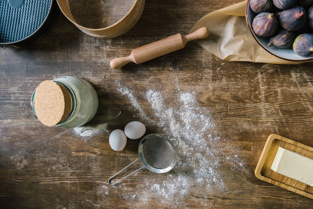 bovenaanzicht van rommelig houten tafel met gemorste meel en bakken ingrediënten - Foto, afbeelding