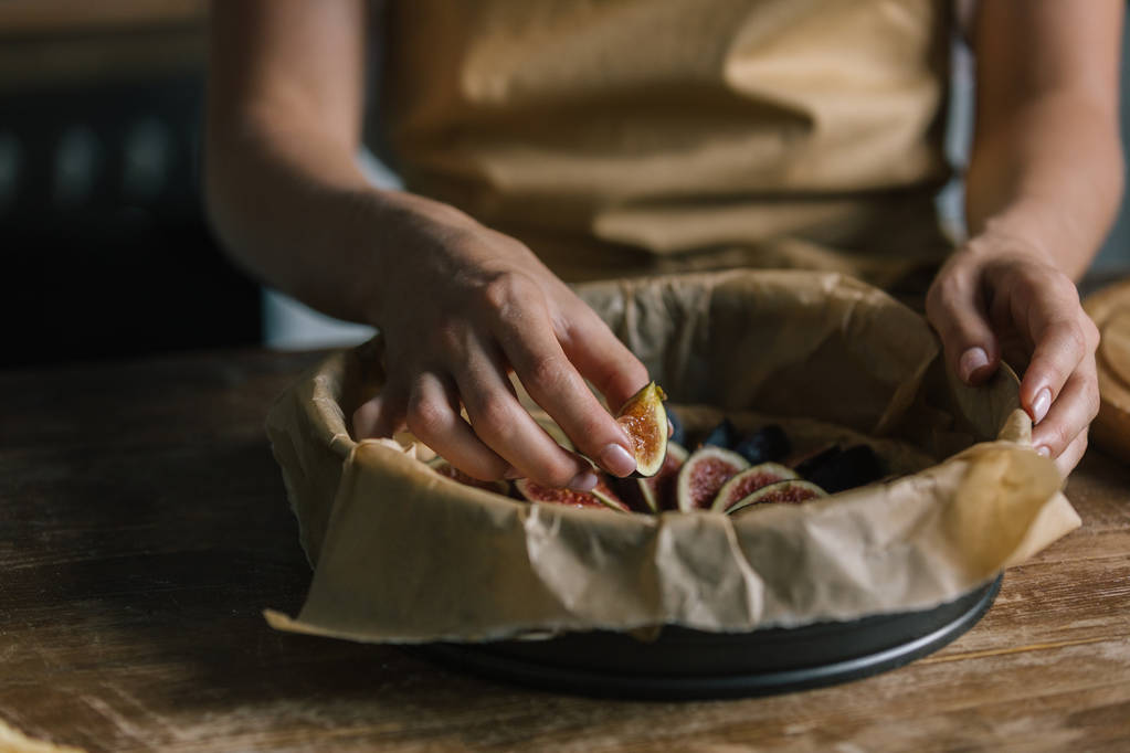 обрезанный снимок женщины, кладущей нарезанный инжир в поднос для выпечки
 - Фото, изображение