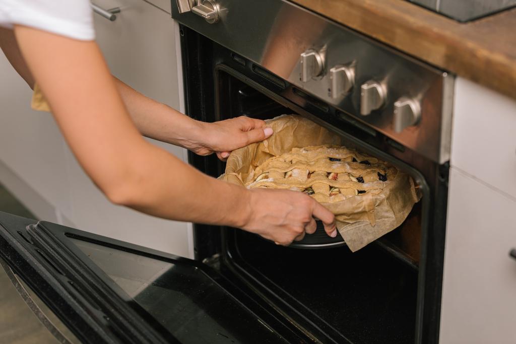 tiro cortado de mulher colocando torta no forno
 - Foto, Imagem