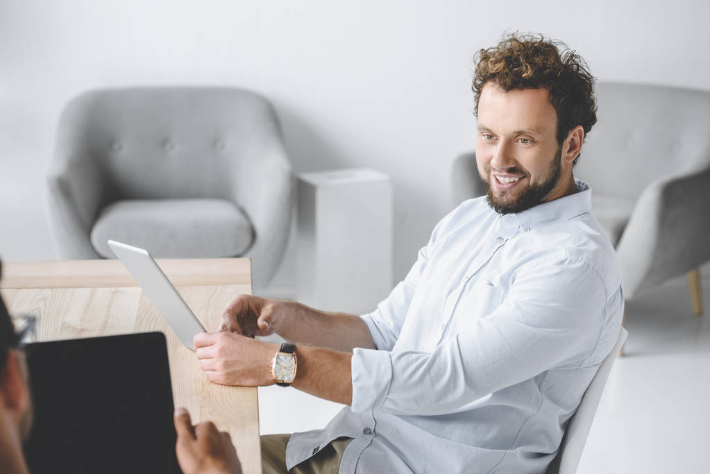 portrait d'un homme d'affaires souriant utilisant une tablette tout en ayant une conversation avec un collègue au bureau
 - Photo, image