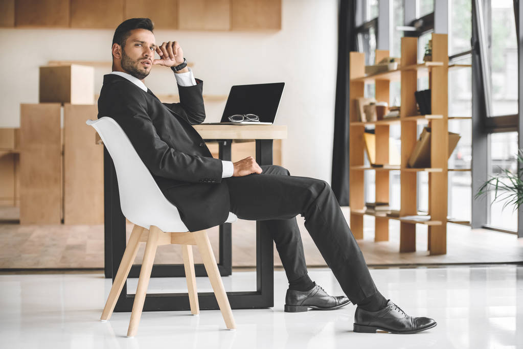 vista lateral de belo empresário sentado no local de trabalho no escritório
 - Foto, Imagem