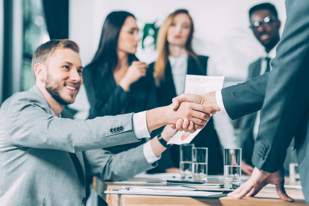 business partners shaking hands with multicultural blurred colleagues on background - Photo, Image