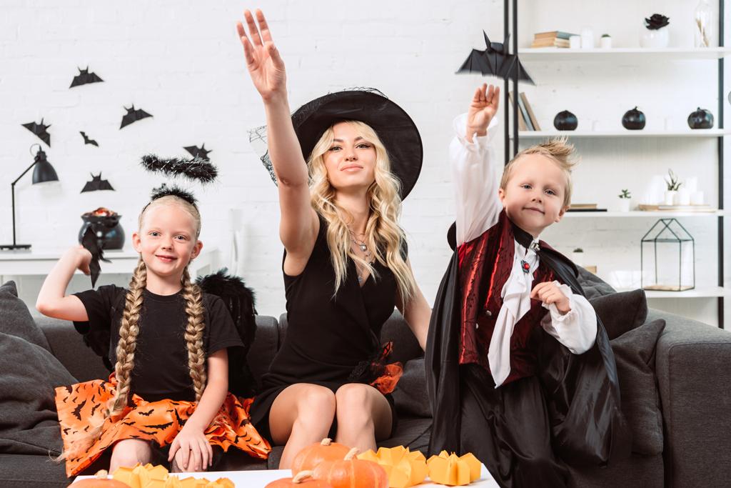 portrait of mother and kids in halloween costumes throwing black paper bats at home - Photo, Image