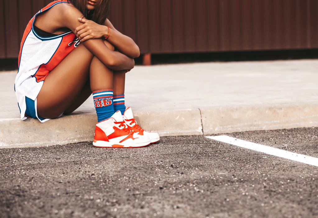 Retrato de modelo de chica hermosa en ropa deportiva de baloncesto rojo sentado en asfalto al aire libre
  - Foto, imagen