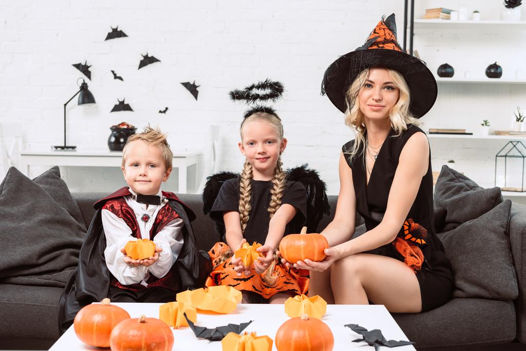 Portrét matky a děti v kostýmech halloween s dýní v rukou sedí na gauči doma - Fotografie, Obrázek