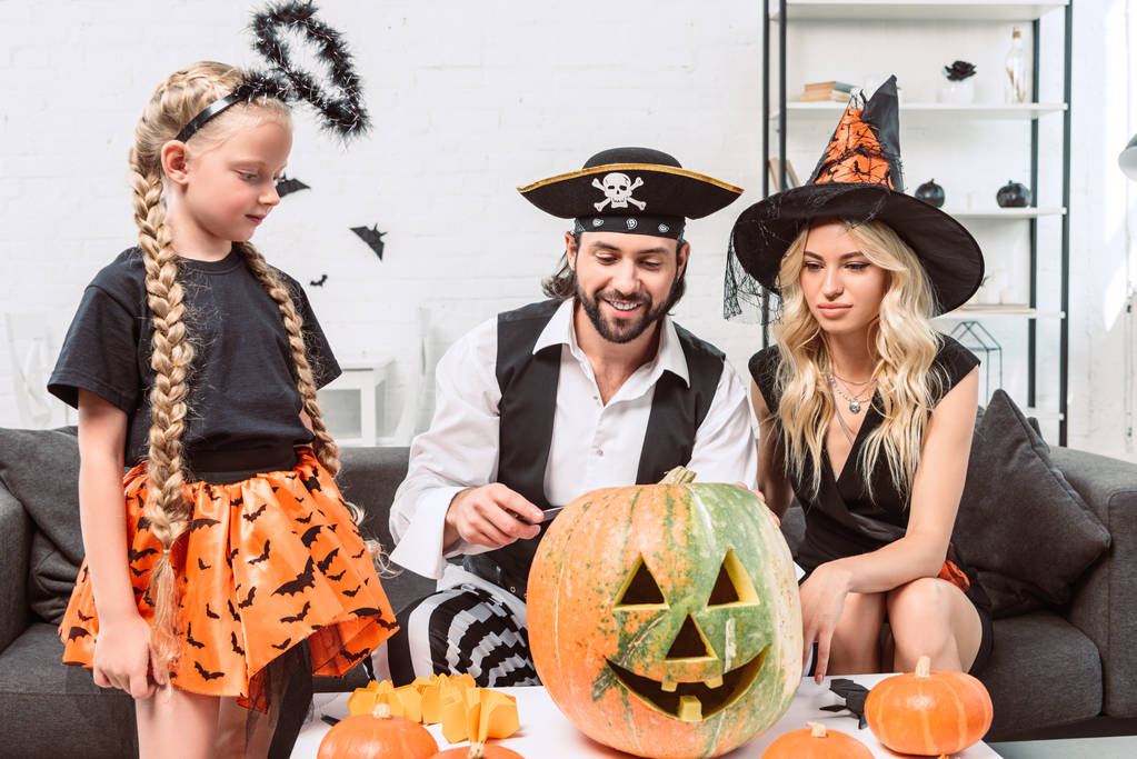 family in halloween costumes on sofa at coffee table with pumpkins at home - Photo, Image