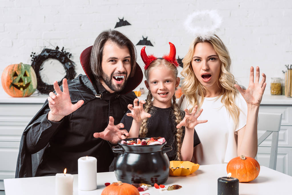 retrato de pais e filha em trajes de Halloween à mesa com guloseimas em panela preta na cozinha em casa
 - Foto, Imagem