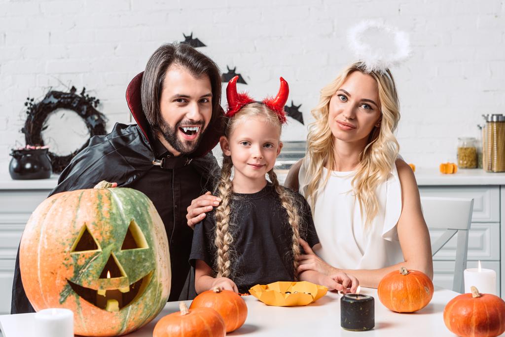 Portret van de familie in de kostuums van halloween aan tafel met pompoenen in keuken thuis - Foto, afbeelding