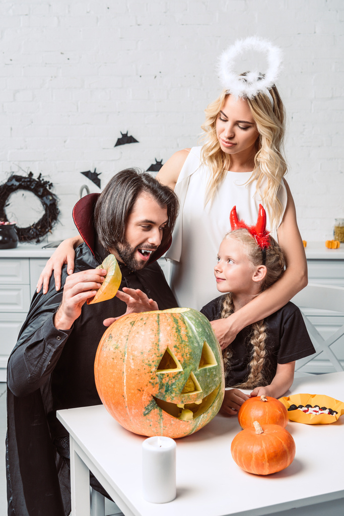 Porträt einer Familie in Halloween-Kostümen am Tisch mit Kürbissen in der heimischen Küche - Foto, Bild