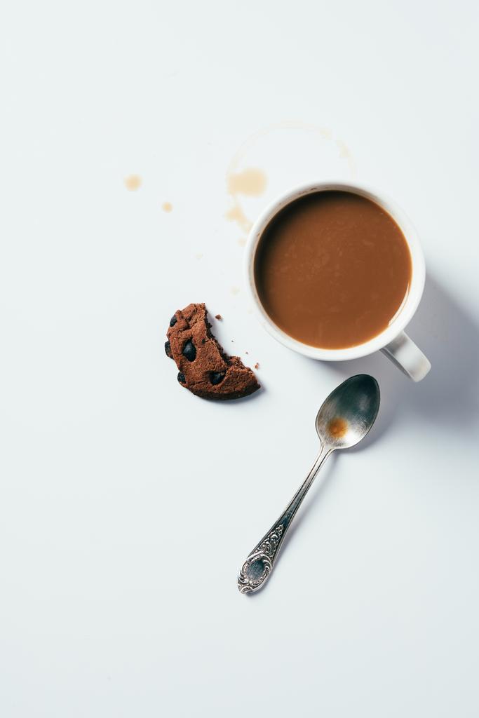 Draufsicht auf Tasse Kaffee mit gebissenem Chocolate Chip Cookie und Löffel auf weißer Oberfläche - Foto, Bild