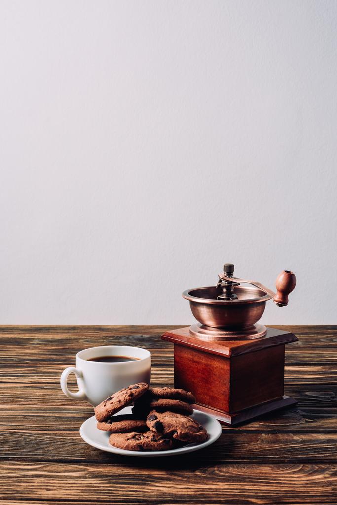 kopje koffie met vintage grinder en chocoladeschilferkoekjes op rustieke houten tafel - Foto, afbeelding