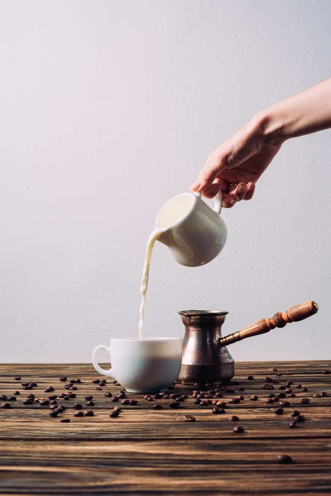 przycięte strzał kobieta wlewając mleko do kawy na rustykalne drewniany stół - Zdjęcie, obraz