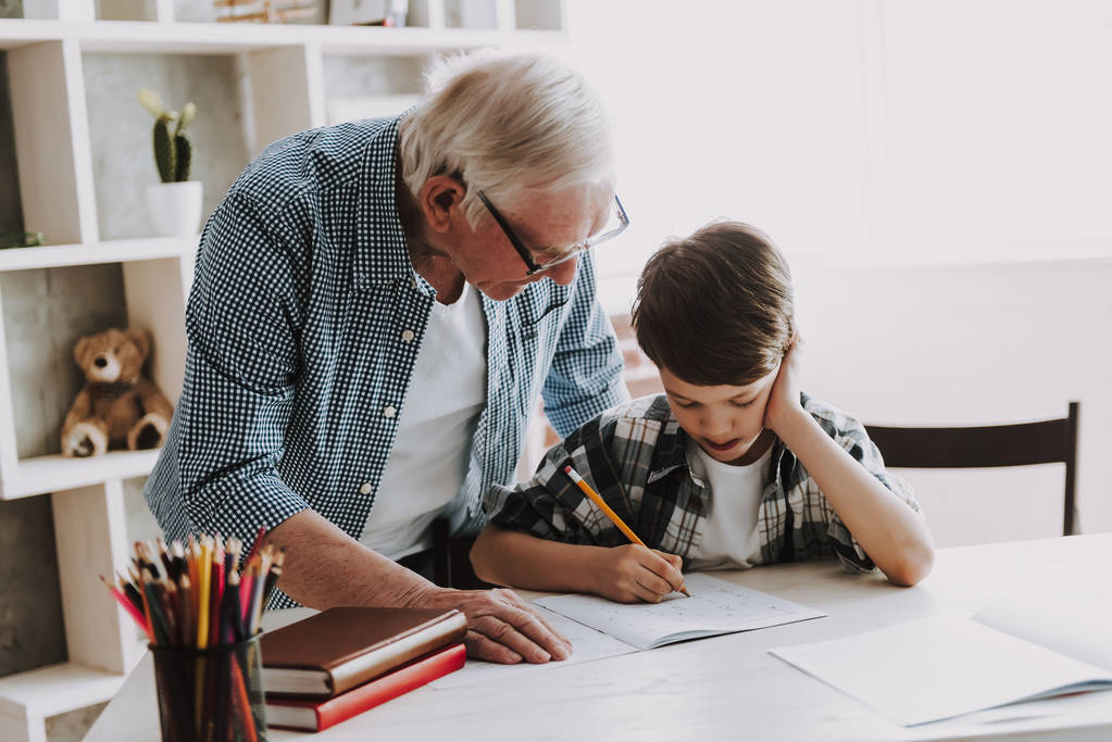 孫は老人ホームで宿題をしている。祖父と孫の家族関係。おじいちゃんの教え、男性の孫、学習コンセプト。関係性と人々の概念. - 写真・画像
