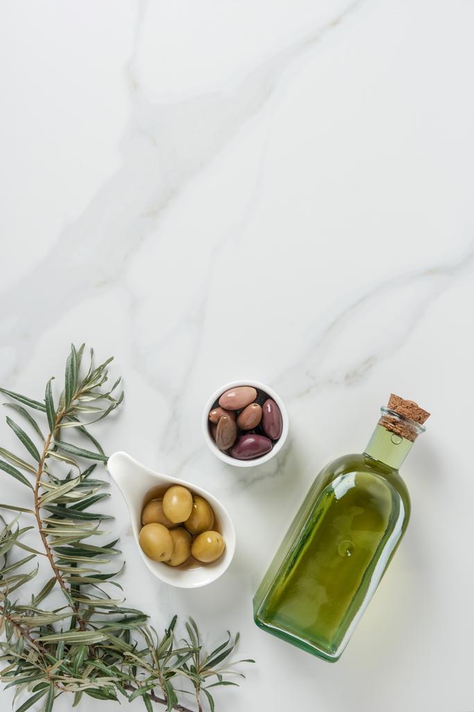 вид сверху на оливковое масло и вкусные оливки в мисках на мраморном столе
  - Фото, изображение