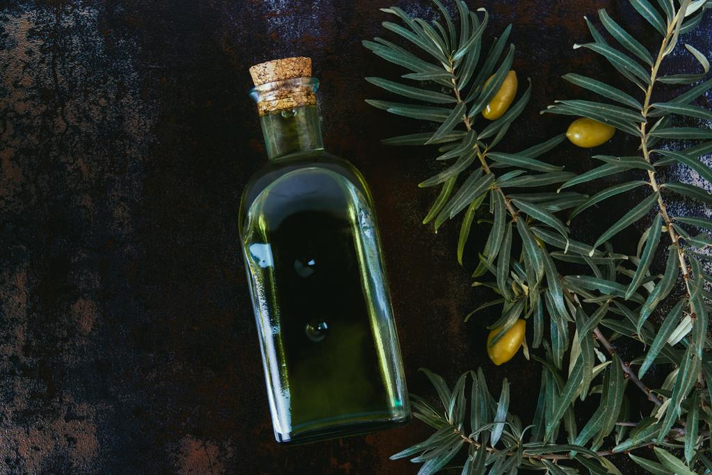 vista superior de la botella de sabroso aceite de oliva, ramitas y aceitunas en la superficie de mala calidad
 - Foto, Imagen