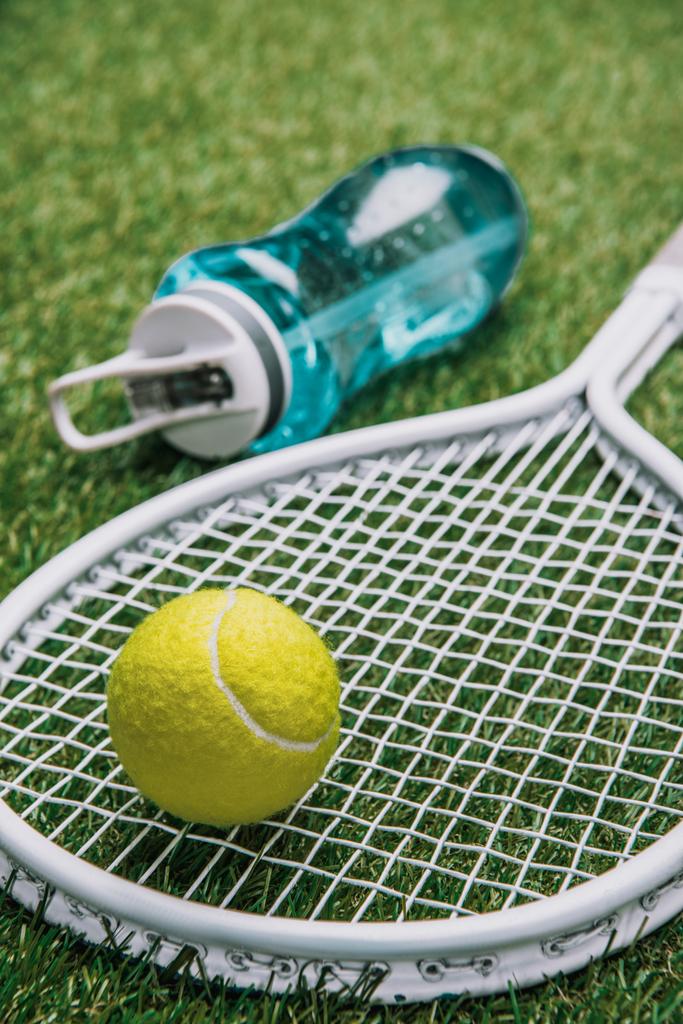 Close-up van tennis apparatuur en sportieve waterfles op groen gras - Foto, afbeelding