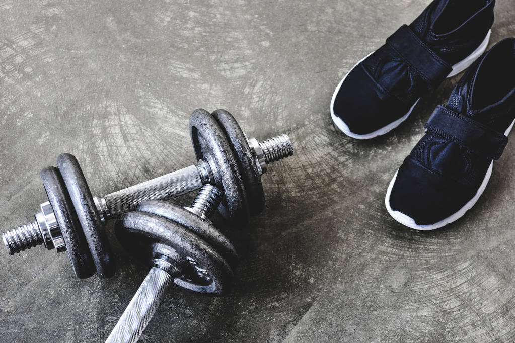 close-up shot of adjustable dumbbells with sneakers on concrete surface - Photo, Image