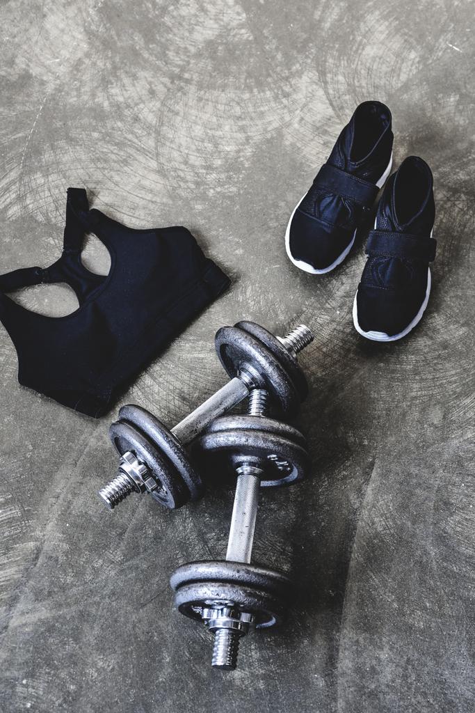 high angle view of dumbbells with sneakers and sport bra on concrete surface - Photo, Image