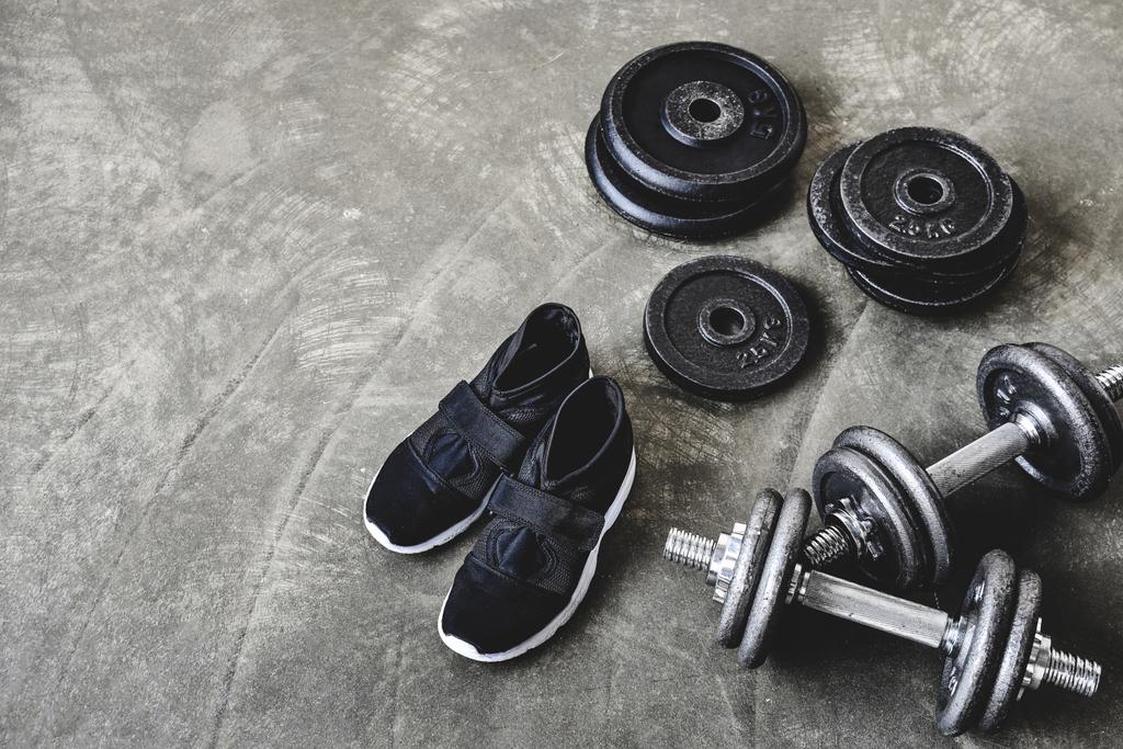 vista de ángulo alto de mancuernas con placas de peso y zapatillas de deporte en el suelo de hormigón
 - Foto, Imagen