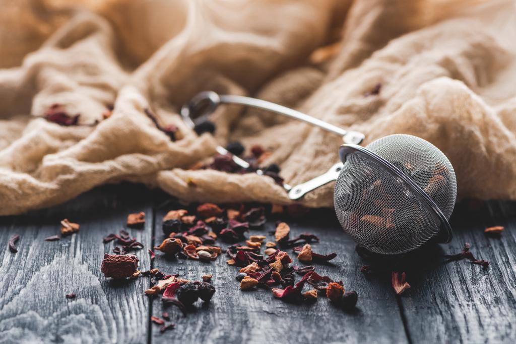 tasty black tea with dried fruits, tea strainer and cloth on wooden table - Photo, Image