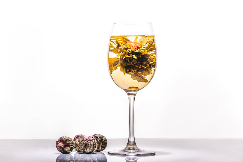 glass of tasty chinese flowering tea with tea balls on reflecting table - Photo, Image