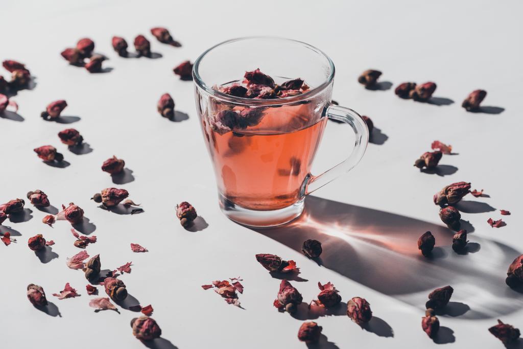 dried rose buds tea in cup and scattered roses on white tabletop - Photo, Image