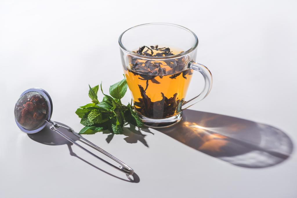 чашка чорного чаю, м'яти і чайної серветки на білому столі
  - Фото, зображення