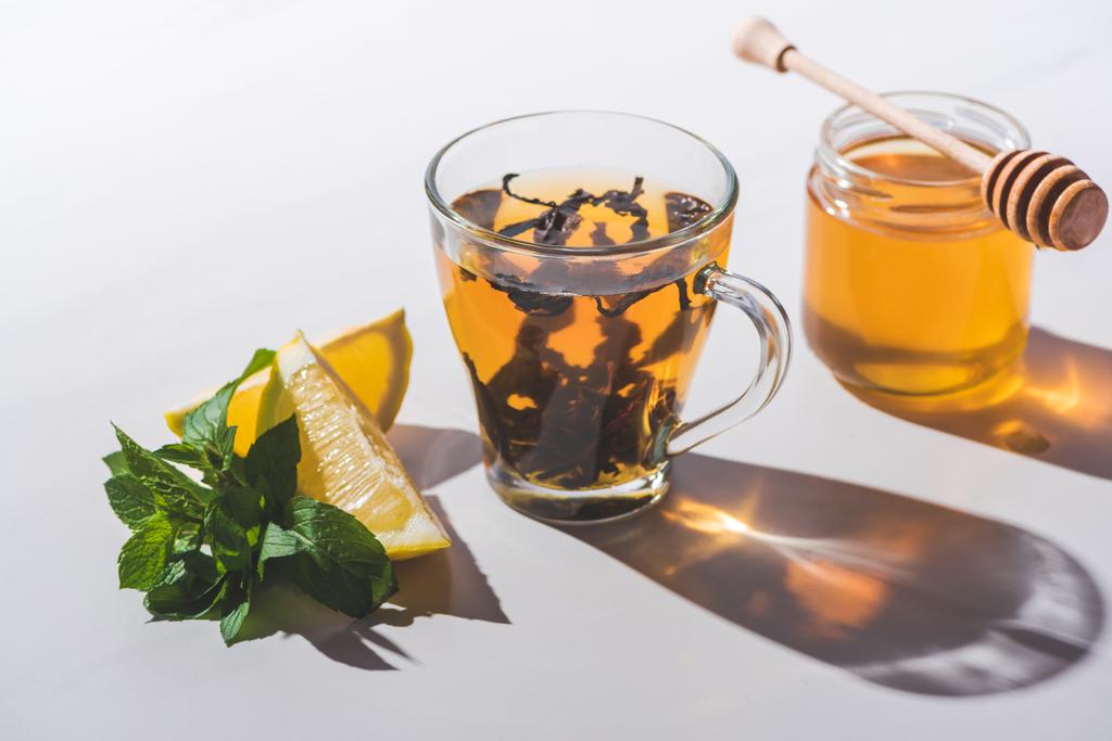 chá preto saudável com mel, limão e hortelã na xícara na mesa branca
 - Foto, Imagem