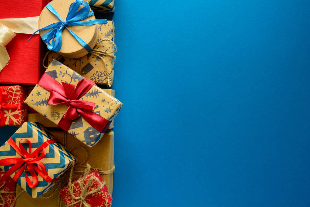 Pohled shora na vánoční dárky zabalený do dárkového papíru zdobené stužkou na modré papírové pozadí. Nový rok, svátky a oslavy dekorace koncept. Kopírovat prostoru. Rozložení bytu - Fotografie, Obrázek