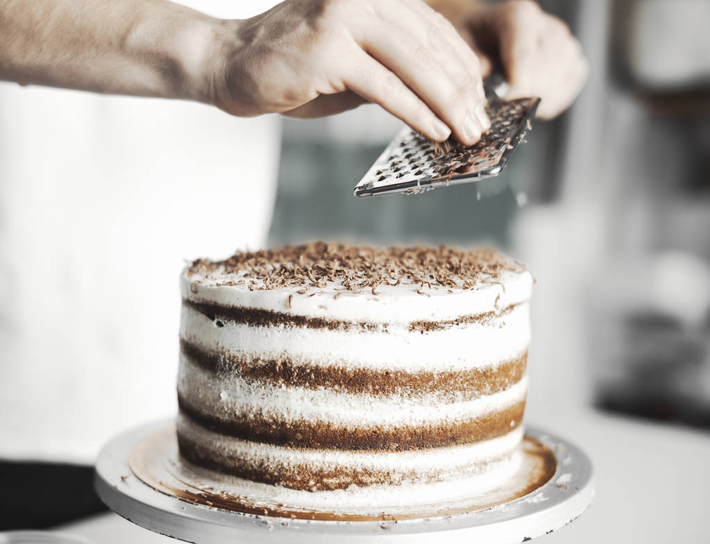 Крупным планом молодой привлекательный повар украшает торт шоколадом
. - Фото, изображение