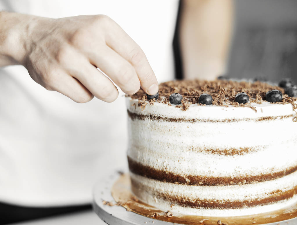 Primo piano di giovane attraente cuoco decorazione torta con bacche
. - Foto, immagini