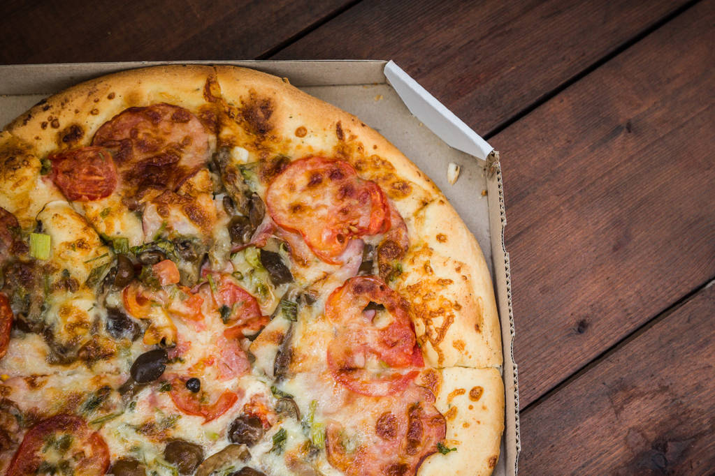 Pizza op houten achtergrond in rustieke stijl. Italiaanse pizza uit de winkel in een kartonnen doos. Eenvoudig eten op een houten achtergrond - Foto, afbeelding