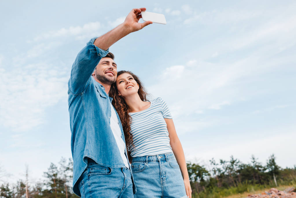 visão inferior do belo casal tirando selfie no smartphone
  - Foto, Imagem