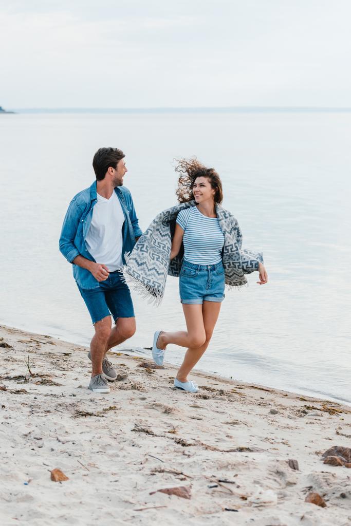 young smiling couple holding hands and running on seashore - Photo, Image