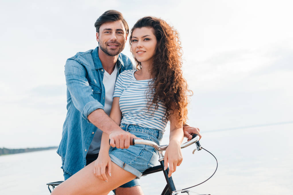 海の近くの自転車に座って幸せな若いカップル - 写真・画像