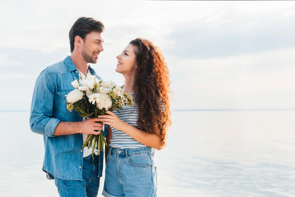 glückliches Paar umarmt und hält Blumenstrauß am Meer  - Foto, Bild