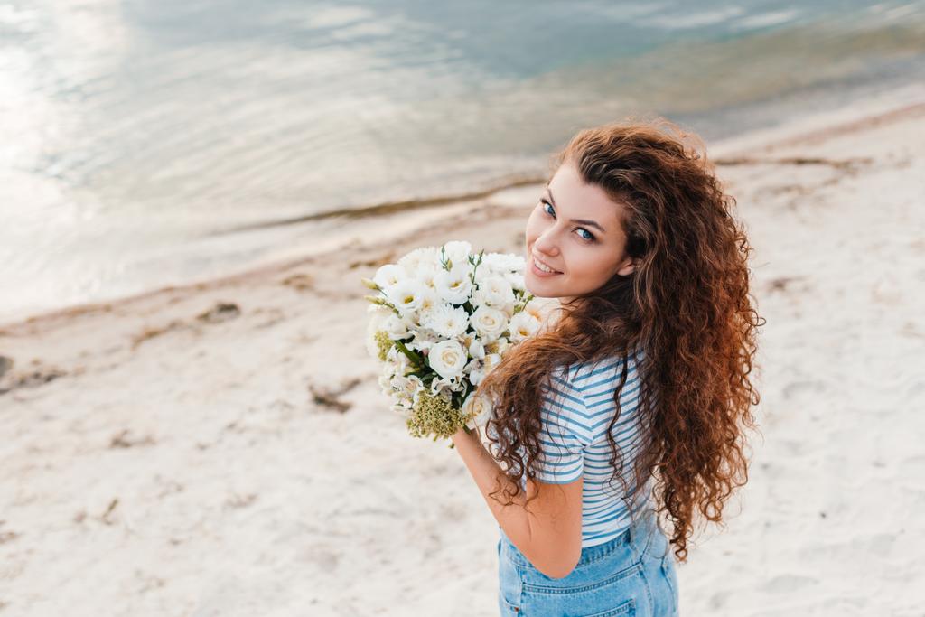 attraente ragazza sorridente con mazzo di fiori in posa sulla spiaggia
 - Foto, immagini
