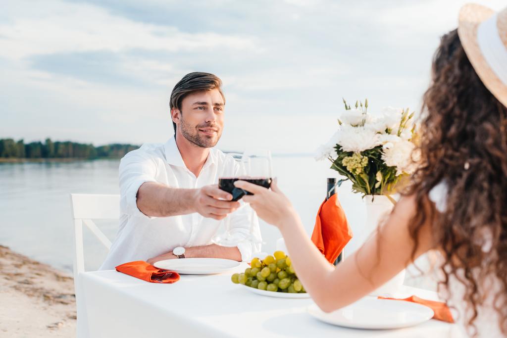 joven pareja tintineo con gafas de vino durante romántica fecha en la playa
 - Foto, imagen