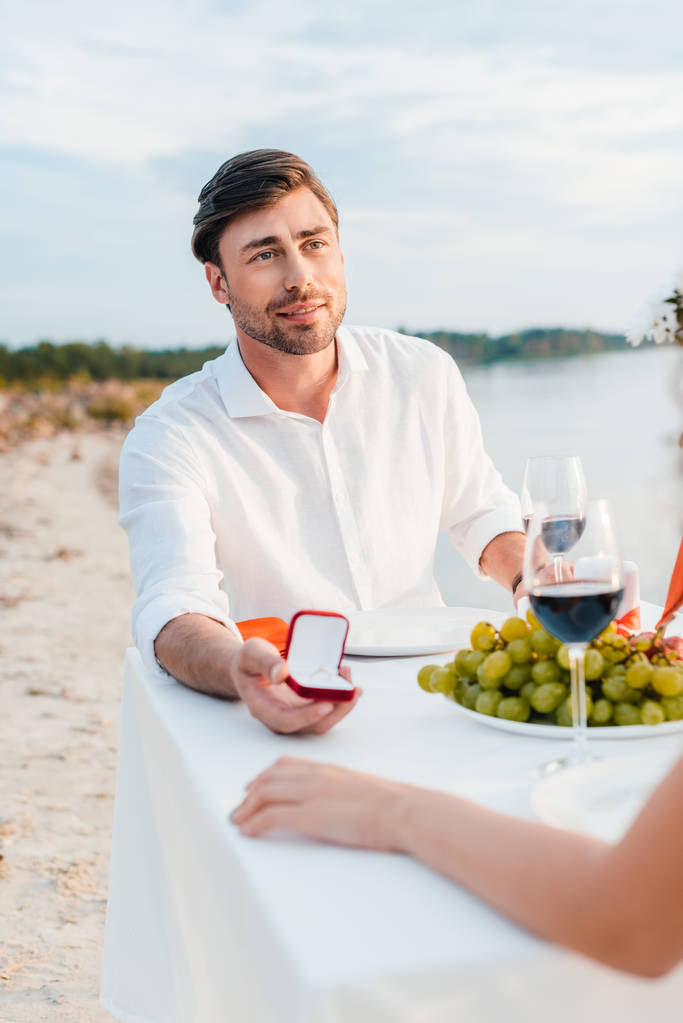 knappe man die voorstellen met ring aan vrouw in romantische datum op strand - Foto, afbeelding