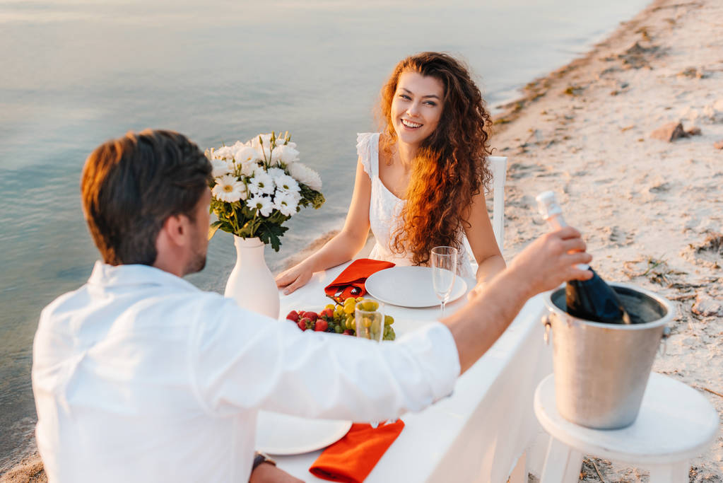 чоловік бере пляшку шампанського на романтичне побачення на пляжі зі усміхненою дівчиною
 - Фото, зображення