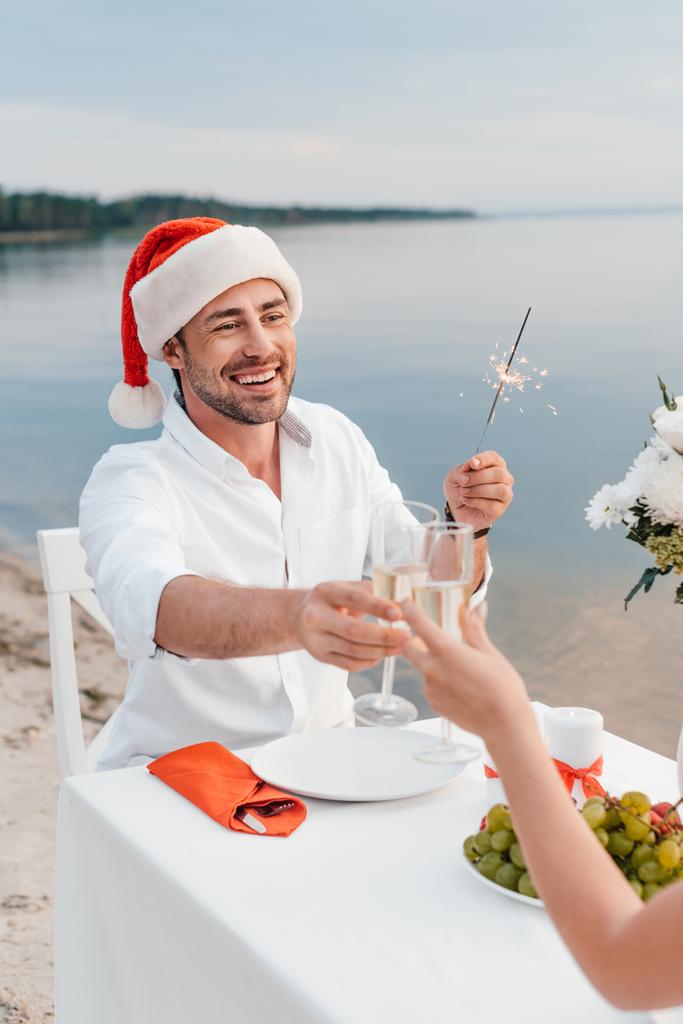 szczęśliwa para obchodzi Boże Narodzenie i brzęk kieliszki do szampana na plaży - Zdjęcie, obraz