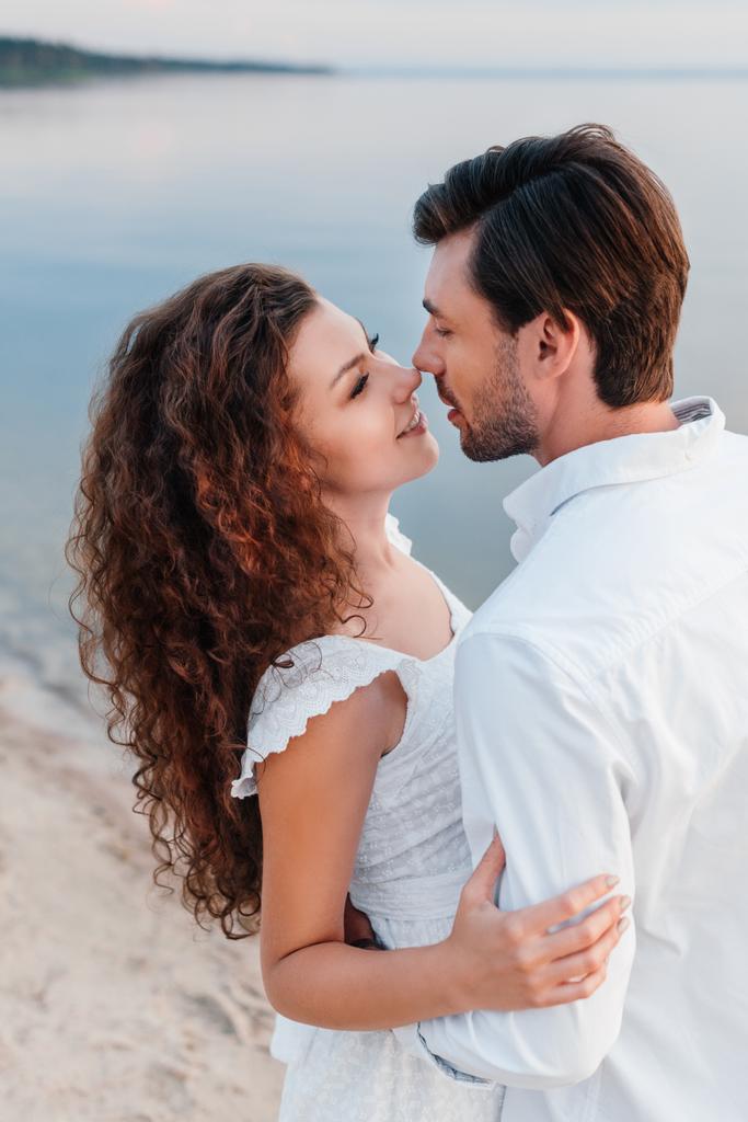 happy romantic couple looking at each other and embracing on seashore - Photo, Image